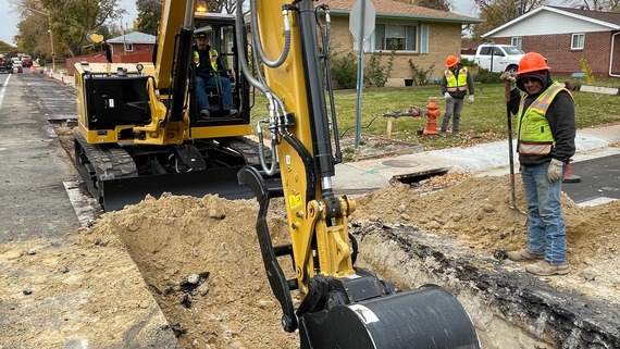 Members of a construction crew use equipment to dig into the street to access a water pipe.