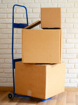 A white brick wall and light-colored wood floor with moving boxes stacked on a dolly