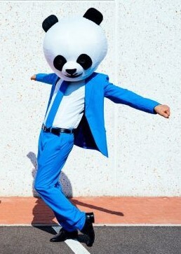 A person dressed in a panda bear costume wearing a bright blue suit appears to dance like Michael Jackson in a parking lot