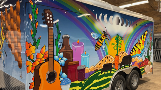 trailer with brightly colored wrap featuring a guitar, a rainbow, bees and rolling hills
