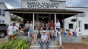 a large group of people stand in front of the Emma Malaby Grocery building