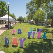 Family Field Day signs in Lincoln Park. Booths and people are in the background.