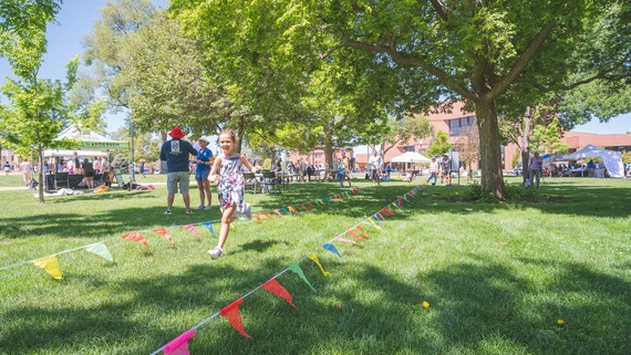 Young girl running down the flagged course at Lincoln Park during Family Field Day with people walking around and talking by booths