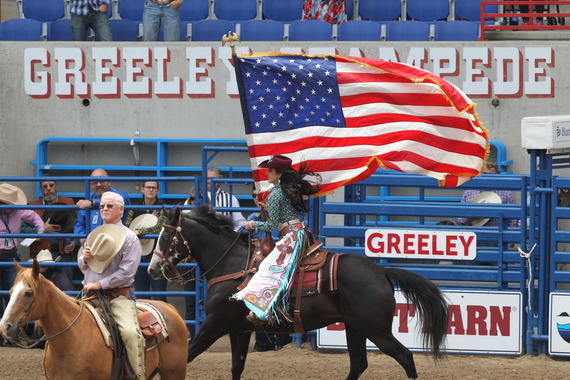 Greeley Stampede rodeo with someone riding horseback in the arena while carrying the United States flag