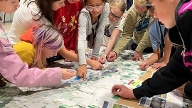 A group of students gather around a map on a table.