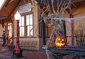 jack-o-lantern on bench in front of yellow train depot at Centennial Village Museum with decorative cornstalks nearby
