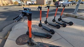 Six SPIN scooters stand in a row on a street corner in downtown Greeley.