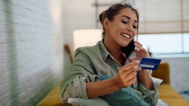 A woman holds a credit card while talking on a cell phone.