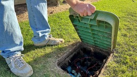 A person holds open an irrigation valve box in the yard.