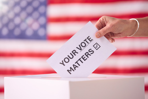 A hand places a card into a box. The card says 'Your Vote Matters'. An American flag is in the background.