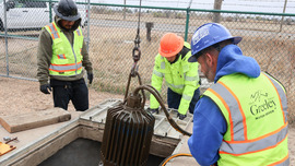 Three workers use a hoist to raise a pump out of a lift station.