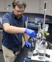 A person wearing gloves and safety glasses performs a test in a lab.
