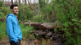 man stands by a log structure in a stream.