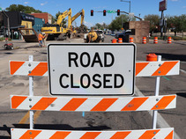 men working in street behind a road closed sign.