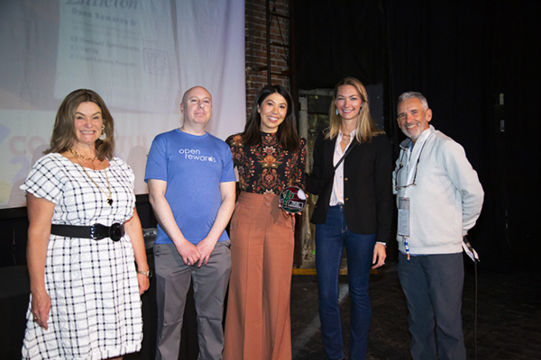 Five adults stand smiling on a stage; one woman in the center holds a Downtown Colorado Inc. award.