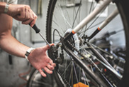 A person adjusts the rear derailleur on a bicycle using a screwdriver, with the bike flipped upside down for maintenance.