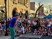 Street performer juggling flaming batons entertains a crowd on a city sidewalk during an outdoor festival