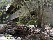 A small waterfall flows over rocks in a landscaped area with trees in front of a concrete building.
