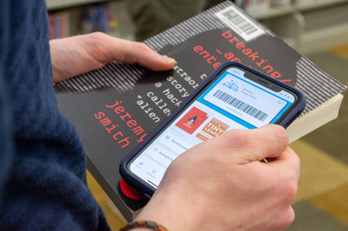 CloudLibrary: person holding book and smartphone, scanning barcode