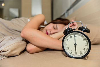 Women asleep with alarm clock on bedside table 