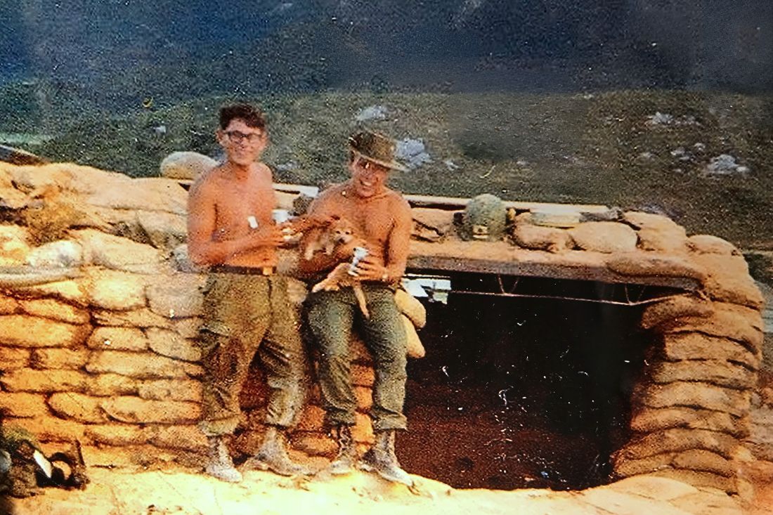 two men in camo pants and no shirts hold a puppy in Vietnam