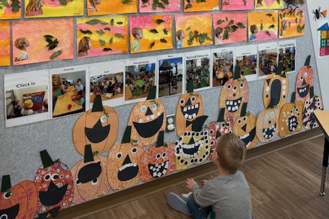young boy looking a preschool art wall