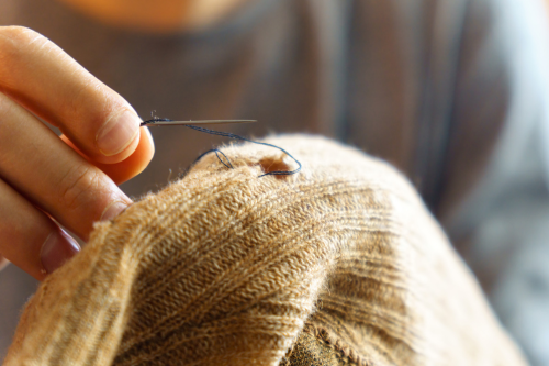 a hand with a needle pushes thread through fabric