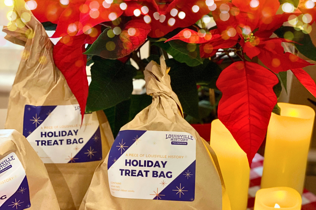 poinsettias and twinkly lights surround brown paper bags with stickers that read "Holiday Treat Bag"