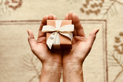 cupped hands hold a brown gift with a bow