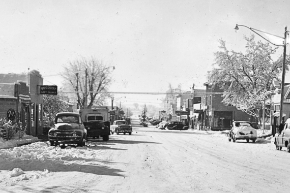 A snowy street scene of Louisville's Main Street with a pine tree in the intersection of Pine and Main