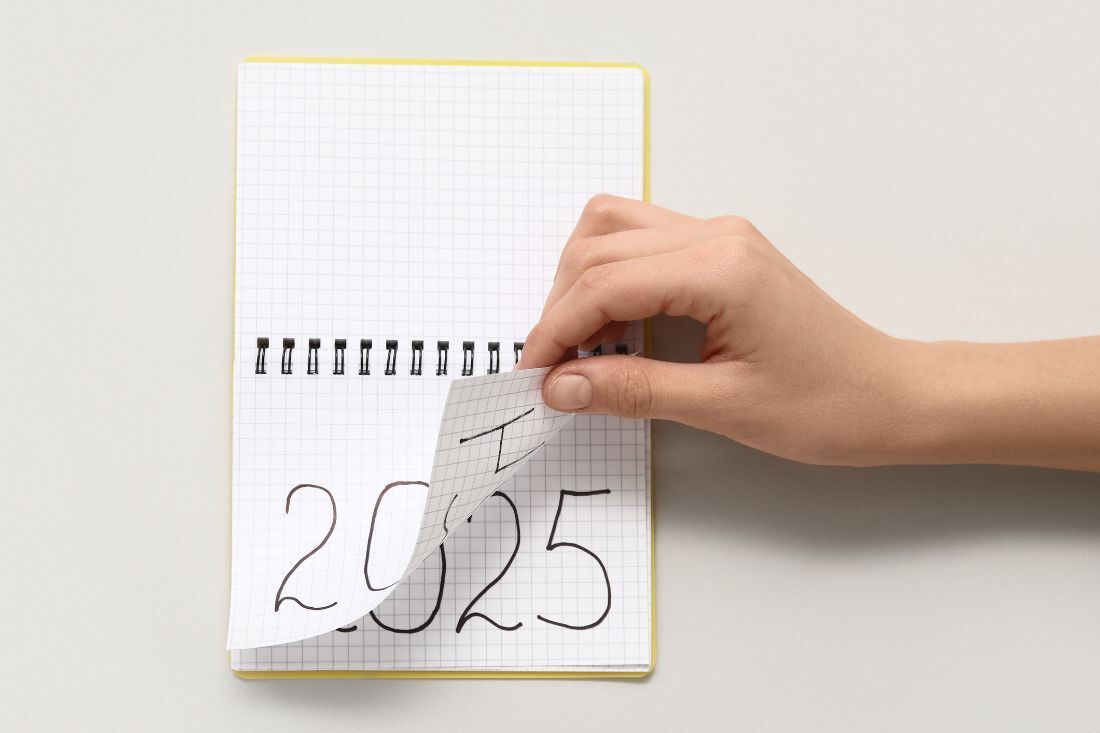 a hand flips a calendar from 2024 to 2025