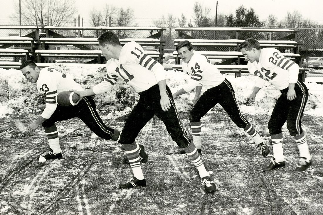 black and white image of four men in Louisville High School football uniforms passing a football