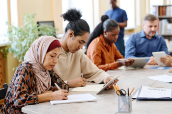 Group of adults writing quietly in public library.