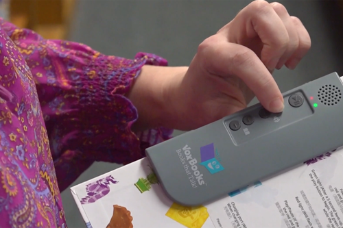 person pressing a button on audio devide on a book to have the story read aloud