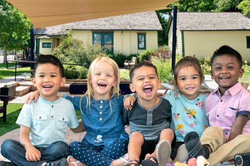 five young children sit, smiling, in front of the Museum courtyard