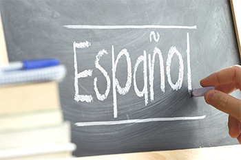 Hand writing on a blackboard in a language class with the word "Spanish" written on it.