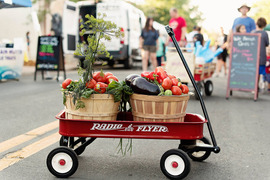 Baskets of produce in a red Radio Flyer wagon in front of a farmers market