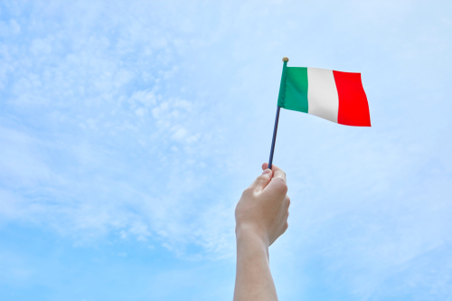 hand waving a small Italian flag against a blue sky