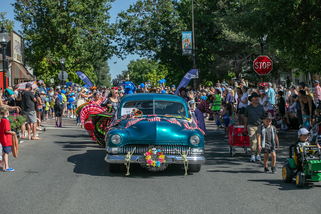 Blue classic car traveling south down Main Street in Louisville, surrounded by crowd at Labor Day parade