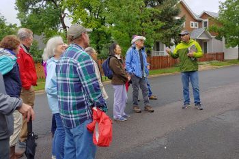 A man leading a group of about ten people on a walking tour on a street in Louisville.