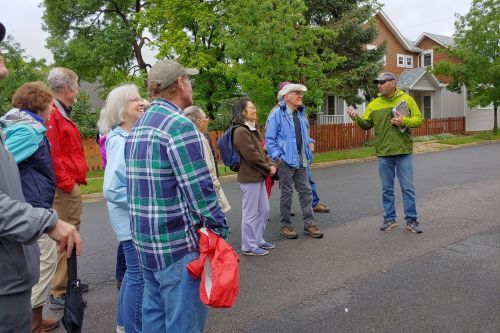Man leading a group of around ten people on a walking tour on a street in Louisville.