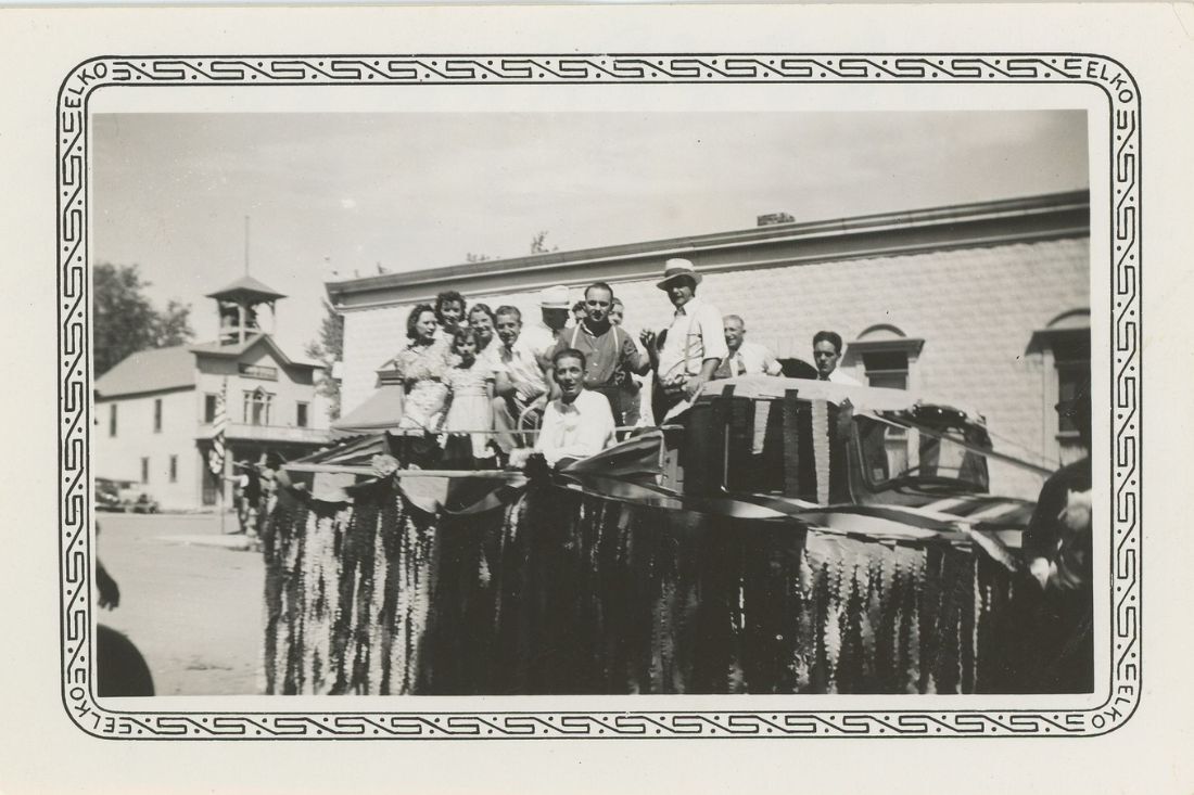 Black and white photo of a group of people standing on a parade float on the corner of Pine and Main Streets in Louisville.