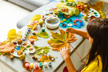 Child painting autumn leaves with various colors of paint.