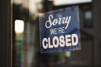 Photo of a sign reading "sorry, we're closed" on a glass door.