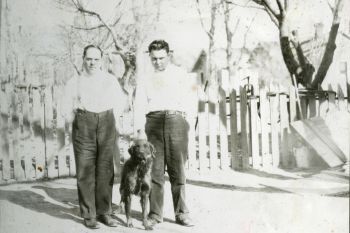 Black and white photo of two men posing with a dog.