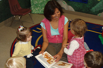 kids sitting in a circle on the floor listening to the teacher read a book