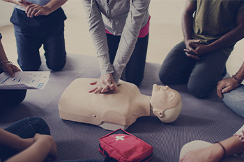 People sitting in a circle while someone practices CPR on a CPR dummy