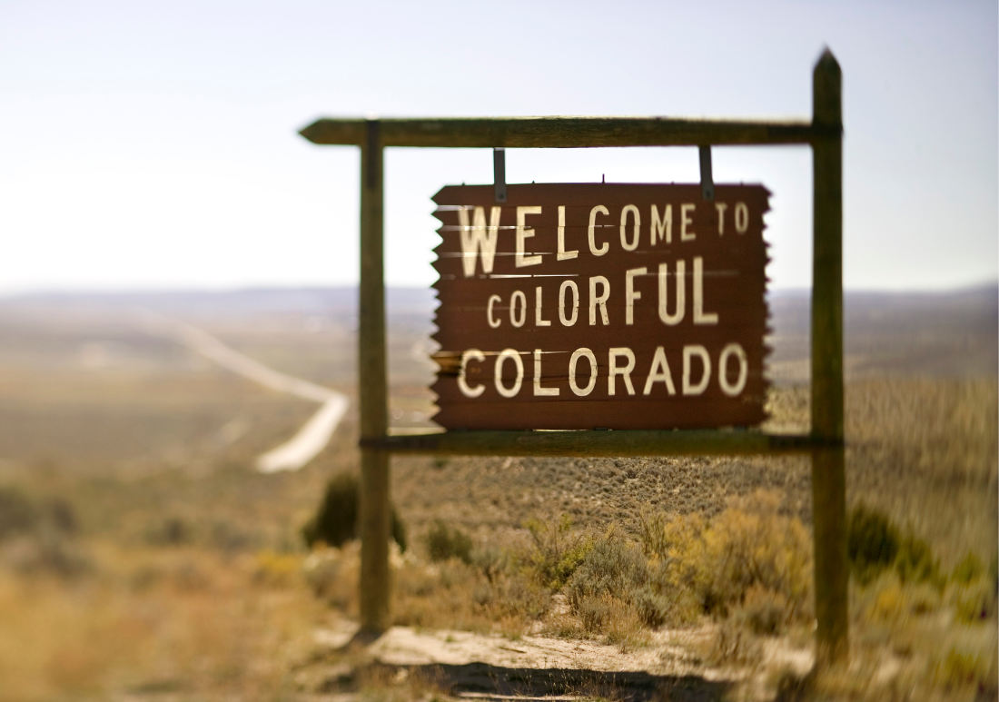 Colorful Colorado welcome sign featuring mountains and vibrant colors against a clear blue sky.