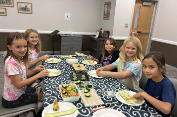 kids sitting at a table learning how to roll sushi
