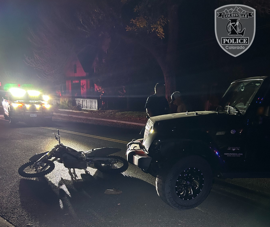 electric motorcycle on the pavement in front of car, headlights illuminating the bike at night
